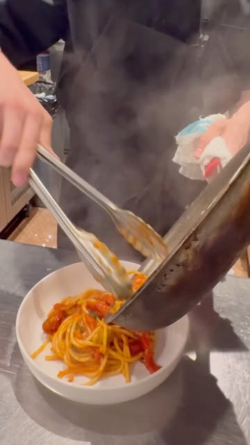 A chef plating spaghetti with cherry tomato sauce straight from the pan at La Bottega