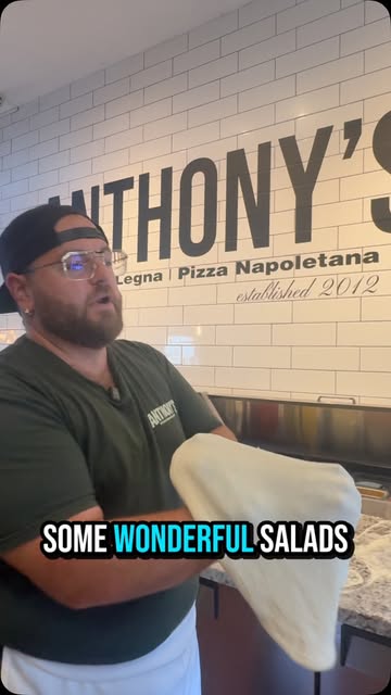 Anthony stretching pizza dough at Anthony's on Wellington, in front of the restaurant's Pizza Napoletana sign