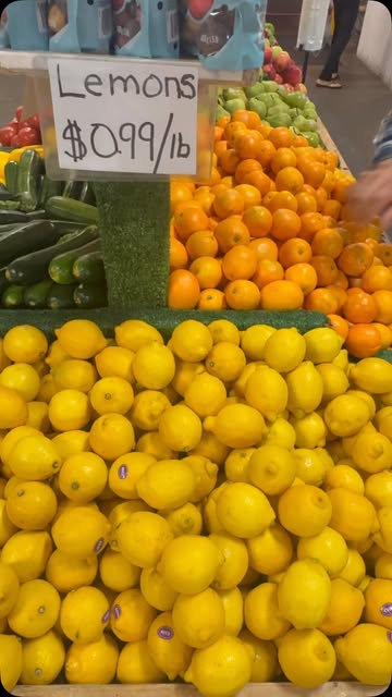 A hand-lettered sign reading Lemons $0.99 a pound, above crates of lemons, oranges and zucchini at the Kaladar Market