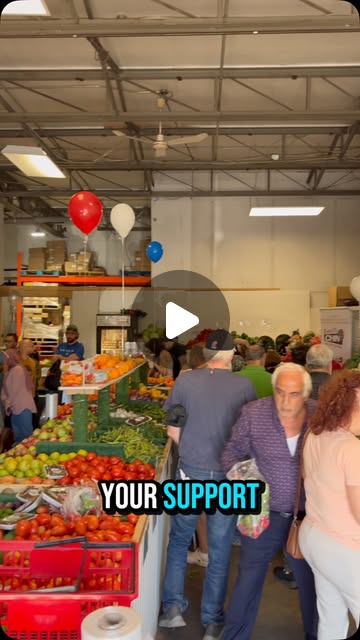 Shoppers filling the aisles of the Kaladar Market on BBQ day, balloons above the produce tables