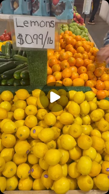 A hand-lettered sign reading Lemons $0.99 a pound above crates of lemons, oranges and zucchini at the Kaladar Market